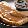 Amandelpasta karamel zeezout uitgesmeerd op een snee brood met een houten spateltje