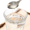 Appelazijn die met een lepel aan een glas water wordt toegevoegd