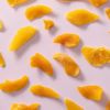 Losse stukjes gedroogde gezoete mango verspreid over een lichtpaarse achtergrond