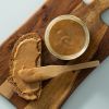 Brood met gemengde notenpasta en een open pot op een houten plank
