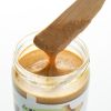 Lepel met smeuïge gemengde notenpasta boven een open pot
