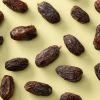Biologische Medjoul dadels los verspreid over een lichtgele achtergrond