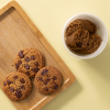 Haverkoeken met chocolade naast een bakje koekjesdeeg op een houten plank