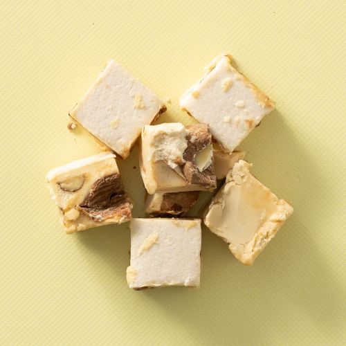 Blokjes soft nougat met kaneelamandelen op een lichtgele achtergrond