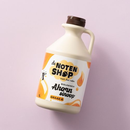 Fles biologische ahornsiroop graad A op een lichtroze achtergrond